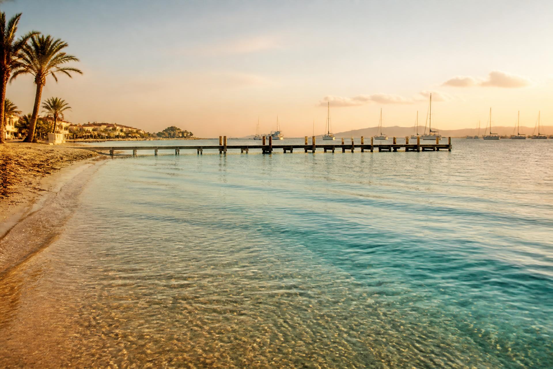 Golden hour over the Mar Menor lagoon at Los Alcázares, with a wooden pier and moored sailing boats